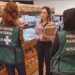 Fiscalização da vigilância sanitária em padaria com agentes conferindo documentos e ASO com a responsável pelo estabelecimento.