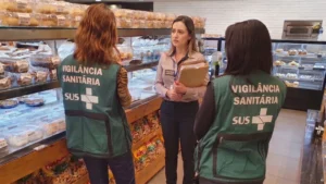Fiscalização da vigilância sanitária em padaria com agentes conferindo documentos e ASO com a responsável pelo estabelecimento.