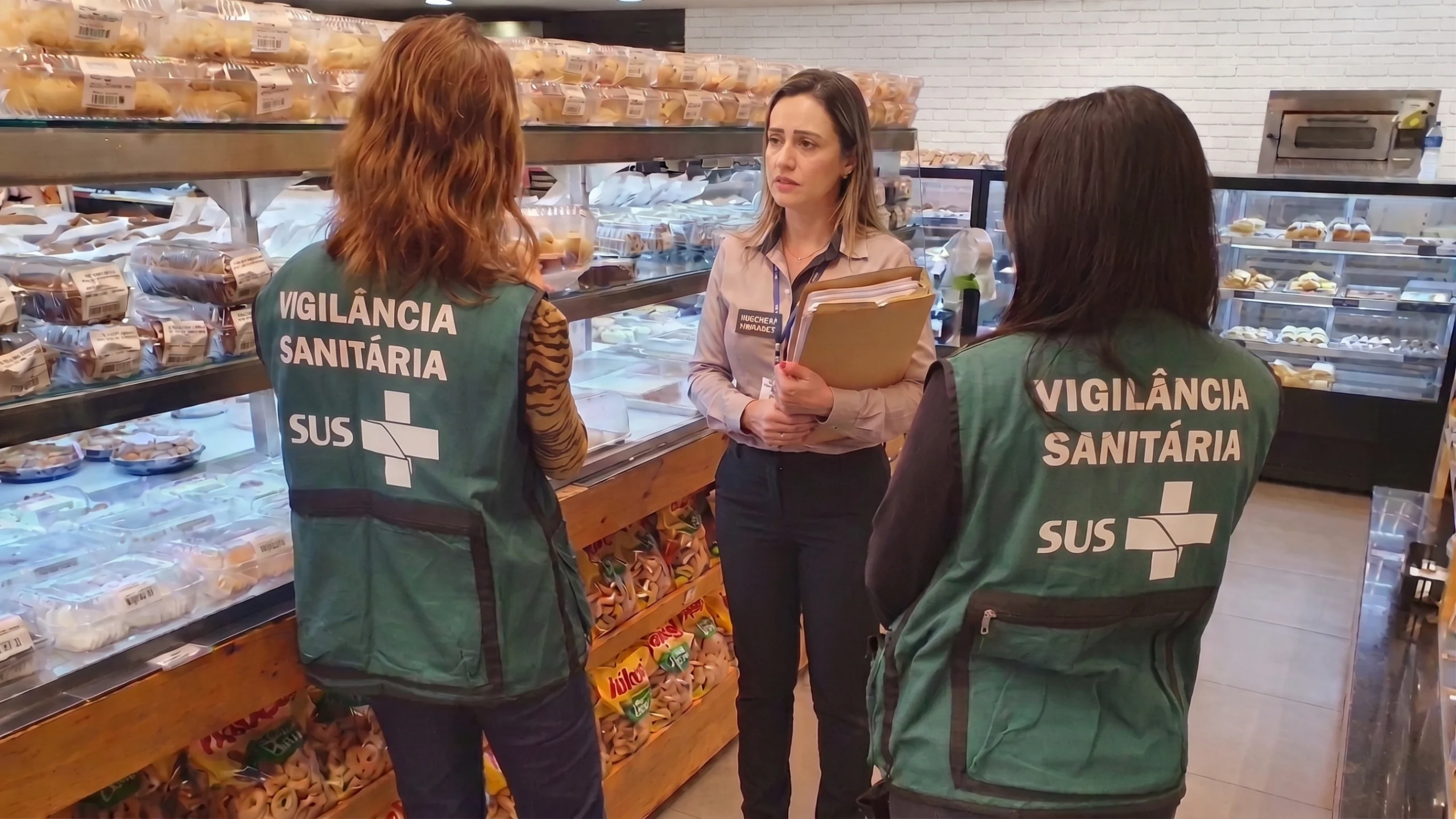 Fiscalização da vigilância sanitária em padaria com agentes conferindo documentos e ASO com a responsável pelo estabelecimento.